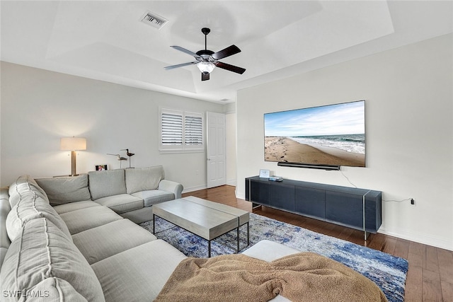 living room featuring ceiling fan, a raised ceiling, and dark wood-type flooring