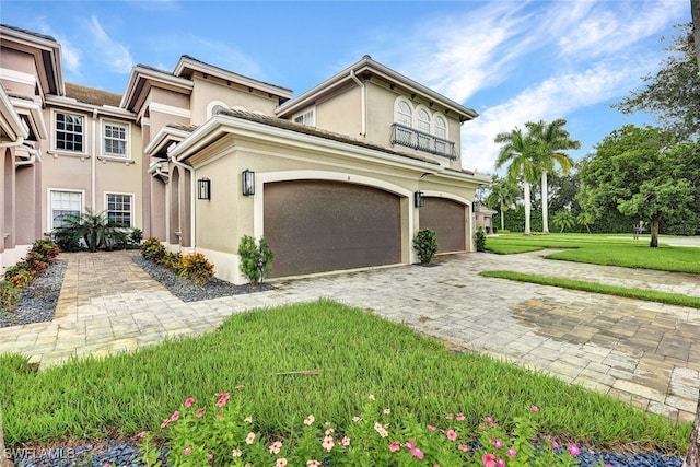 view of front facade with stucco siding, decorative driveway, a front lawn, and an attached garage