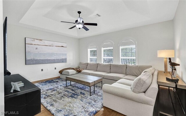 living room featuring ceiling fan, a raised ceiling, and wood-type flooring