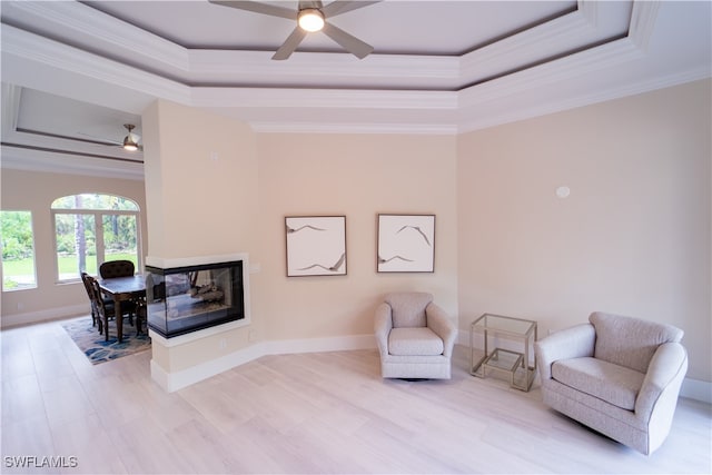 sitting room featuring a multi sided fireplace, ornamental molding, a tray ceiling, and ceiling fan