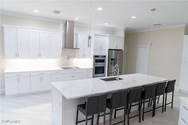 kitchen featuring wall chimney exhaust hood, an island with sink, stainless steel appliances, sink, and white cabinetry