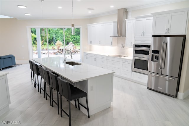 kitchen with appliances with stainless steel finishes, sink, an island with sink, white cabinetry, and wall chimney exhaust hood