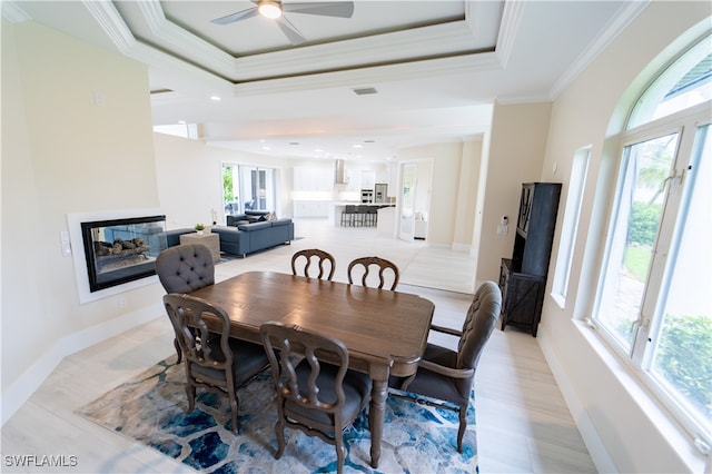 dining room featuring a multi sided fireplace, ornamental molding, a tray ceiling, and ceiling fan