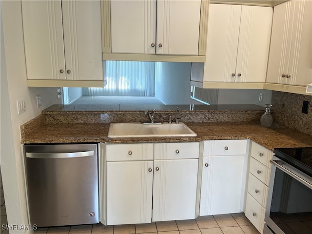 kitchen featuring appliances with stainless steel finishes, sink, white cabinets, light tile patterned floors, and dark stone countertops