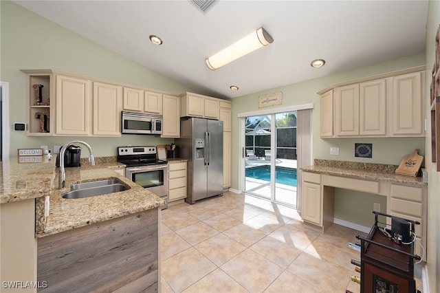 kitchen with sink, stainless steel appliances, vaulted ceiling, and cream cabinetry