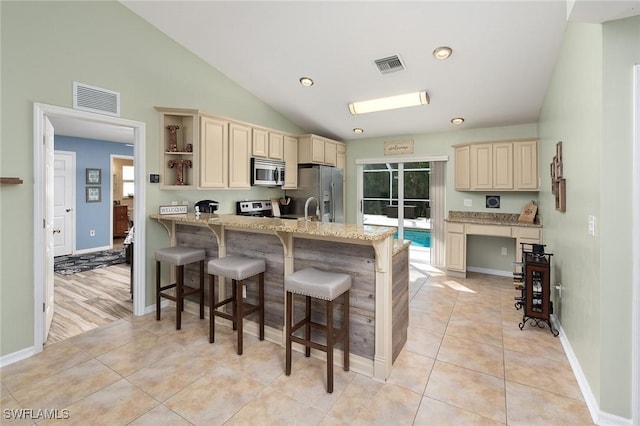 kitchen featuring a breakfast bar, stainless steel appliances, light stone counters, cream cabinets, and light tile patterned flooring