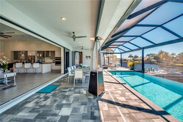 view of pool featuring a lanai, ceiling fan, a water view, a patio area, and an outdoor bar