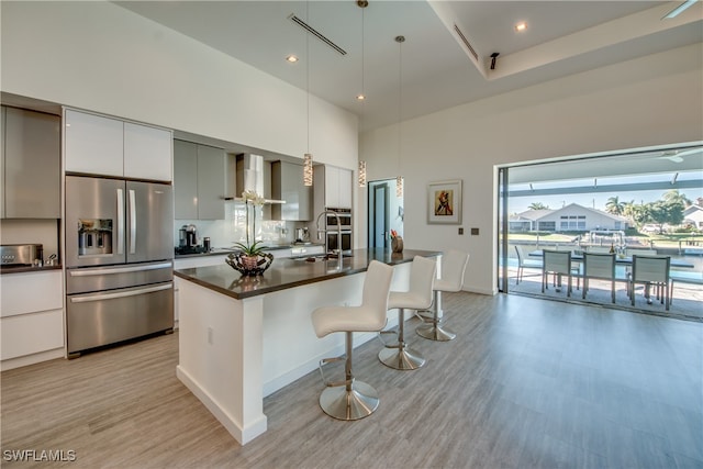 kitchen with pendant lighting, a breakfast bar, wall chimney range hood, a towering ceiling, and stainless steel fridge with ice dispenser