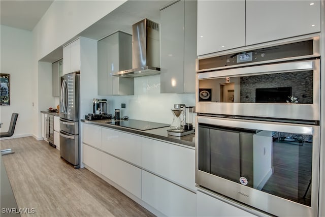 kitchen featuring decorative backsplash, appliances with stainless steel finishes, wall chimney exhaust hood, light hardwood / wood-style flooring, and white cabinetry