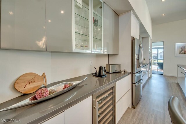 bar featuring stainless steel fridge with ice dispenser, light hardwood / wood-style floors, white cabinetry, and beverage cooler