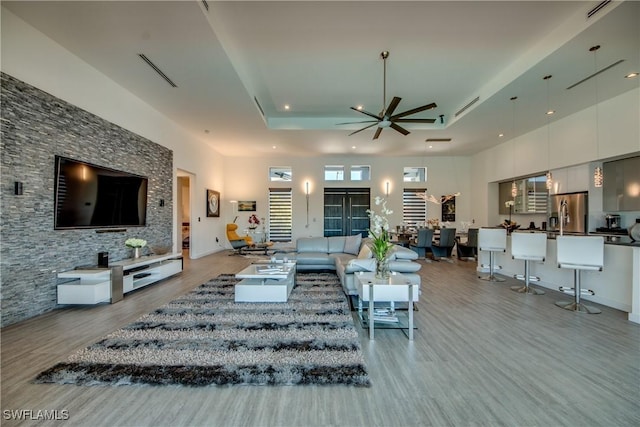 living area featuring light wood-style floors, a raised ceiling, ceiling fan, and a towering ceiling