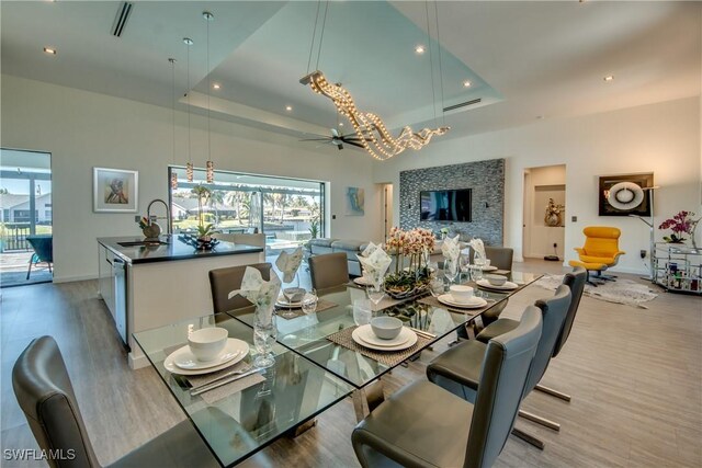 dining area featuring a high ceiling, ceiling fan with notable chandelier, a raised ceiling, and wood-type flooring