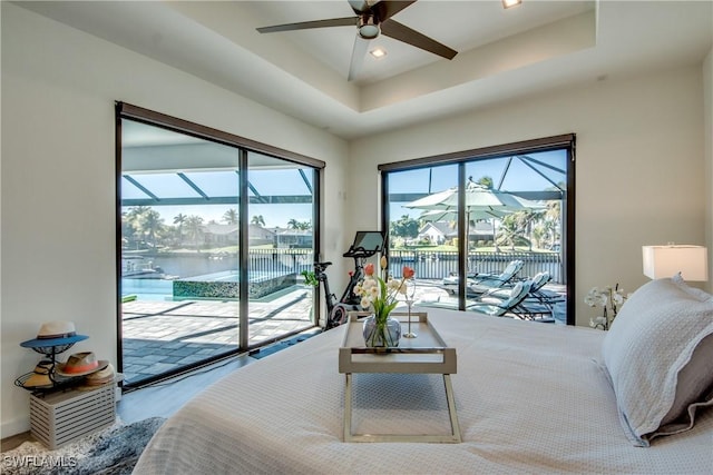 bedroom featuring recessed lighting, a water view, a sunroom, access to outside, and a tray ceiling