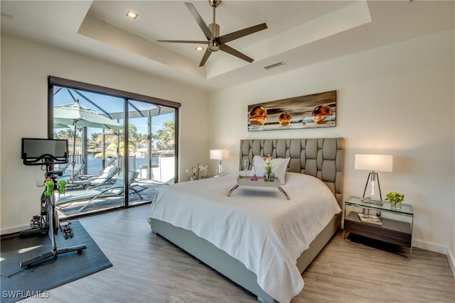 bedroom with ceiling fan, a tray ceiling, access to outside, and light hardwood / wood-style flooring