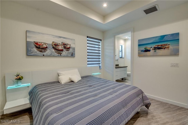 bedroom with a raised ceiling, wood finished floors, visible vents, and baseboards