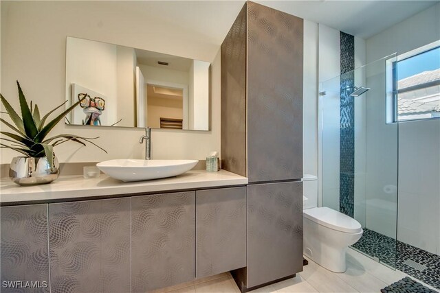 bathroom featuring tile patterned flooring, a tile shower, vanity, and toilet