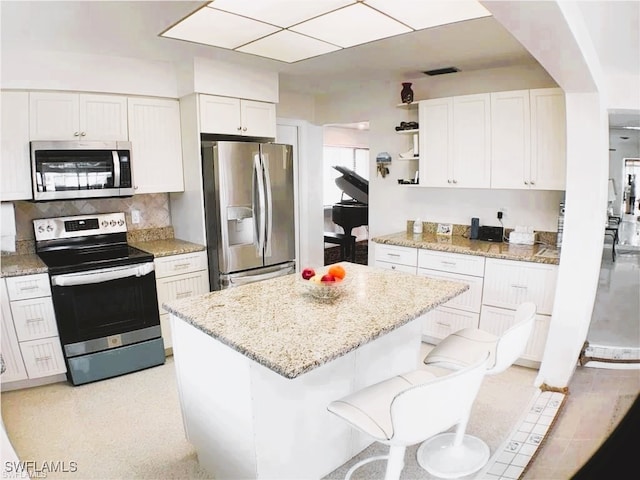 kitchen with a kitchen bar, light stone countertops, stainless steel appliances, and white cabinets