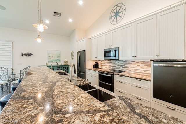 kitchen with dark stone countertops, backsplash, pendant lighting, stainless steel appliances, and white cabinets