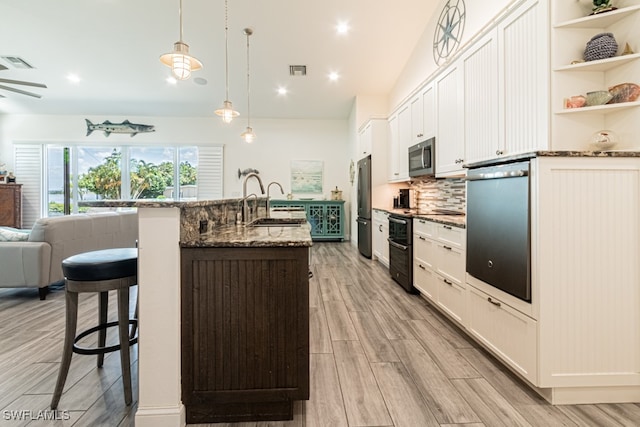 kitchen featuring appliances with stainless steel finishes, dark stone countertops, white cabinets, a kitchen bar, and decorative light fixtures