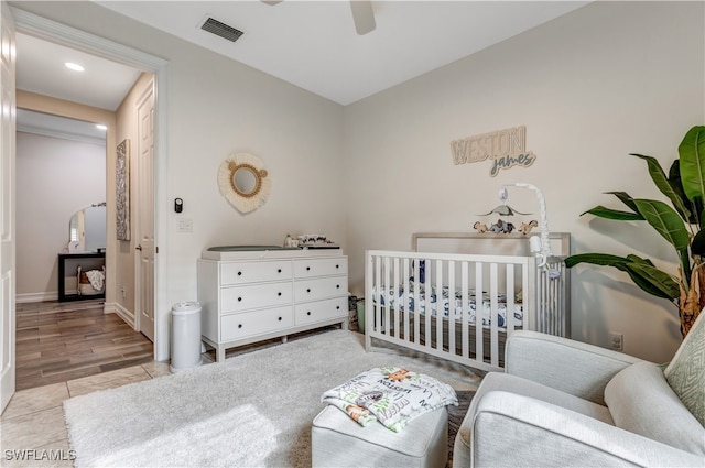 bedroom featuring ceiling fan, light hardwood / wood-style floors, and a nursery area