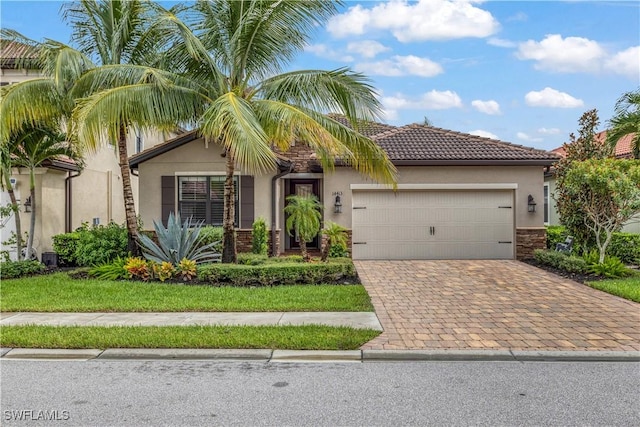 view of front of property featuring an attached garage, stucco siding, stone siding, a tiled roof, and decorative driveway