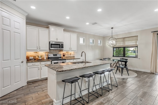 kitchen with appliances with stainless steel finishes, light stone counters, sink, white cabinets, and an island with sink