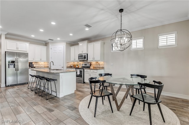 kitchen with stainless steel appliances, light stone counters, a notable chandelier, an island with sink, and white cabinets