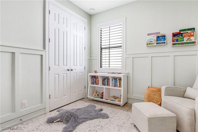 sitting room featuring light tile patterned floors, a decorative wall, and a wainscoted wall