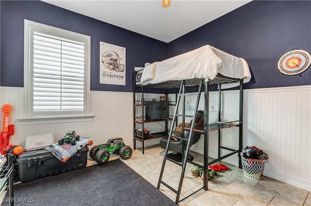 bedroom with tile patterned flooring and a wainscoted wall