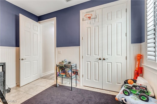 recreation room featuring tile patterned flooring, wainscoting, and carpet floors