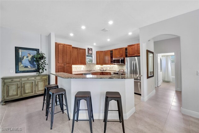 kitchen featuring arched walkways, decorative backsplash, a kitchen breakfast bar, a center island, and stainless steel appliances