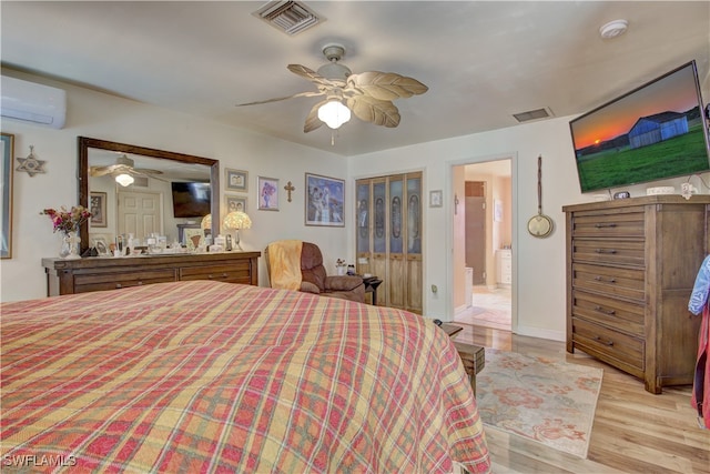 bedroom with an AC wall unit, ensuite bath, ceiling fan, and light hardwood / wood-style flooring