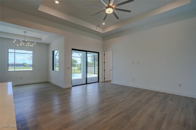 unfurnished room with dark hardwood / wood-style flooring, ceiling fan with notable chandelier, a tray ceiling, and a healthy amount of sunlight