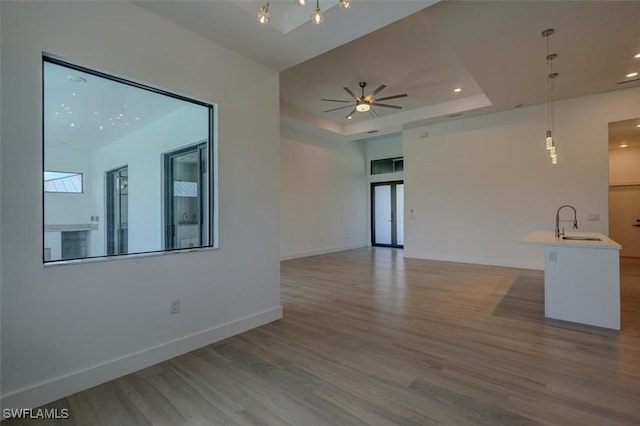 unfurnished living room with ceiling fan, light wood-type flooring, sink, and a tray ceiling