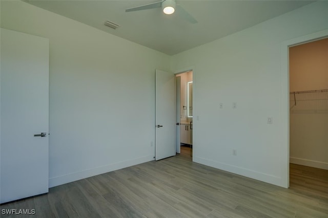 unfurnished bedroom with a walk in closet, ceiling fan, a closet, and light hardwood / wood-style floors