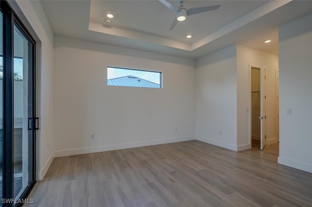 empty room featuring ceiling fan, light hardwood / wood-style floors, and a tray ceiling