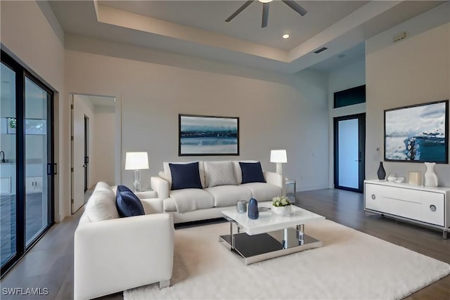 living room with hardwood / wood-style flooring, ceiling fan, a raised ceiling, and a high ceiling