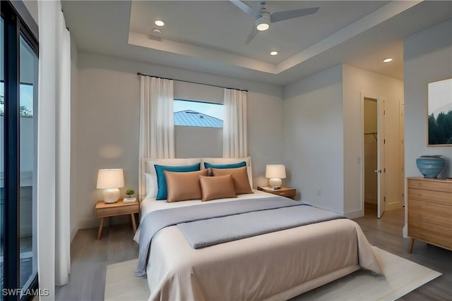 bedroom featuring ceiling fan, wood-type flooring, and a tray ceiling