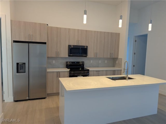 kitchen with hanging light fixtures, stainless steel appliances, a kitchen island with sink, and sink