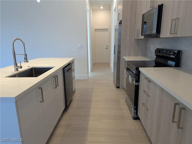 kitchen featuring appliances with stainless steel finishes, light wood-type flooring, light brown cabinetry, a kitchen island with sink, and sink