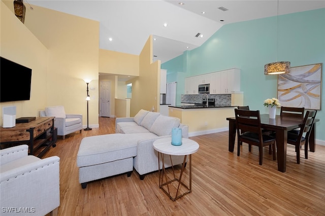 living room with light hardwood / wood-style flooring, sink, and high vaulted ceiling