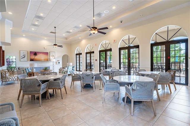 tiled dining space featuring french doors, crown molding, ceiling fan, a raised ceiling, and a towering ceiling