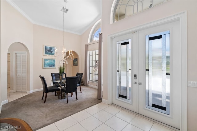 carpeted dining room with french doors, a towering ceiling, crown molding, and a chandelier