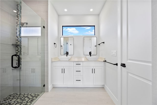 bathroom featuring double sink vanity, a shower with shower door, and a healthy amount of sunlight