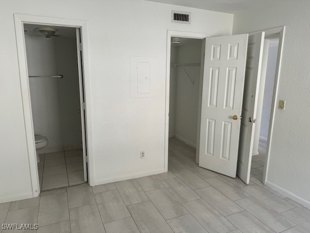 unfurnished bedroom with ensuite bathroom, a spacious closet, electric panel, and a closet