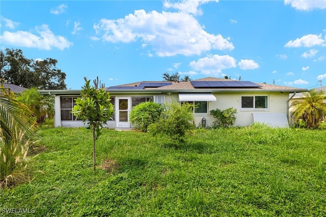 back of property with a lawn and solar panels