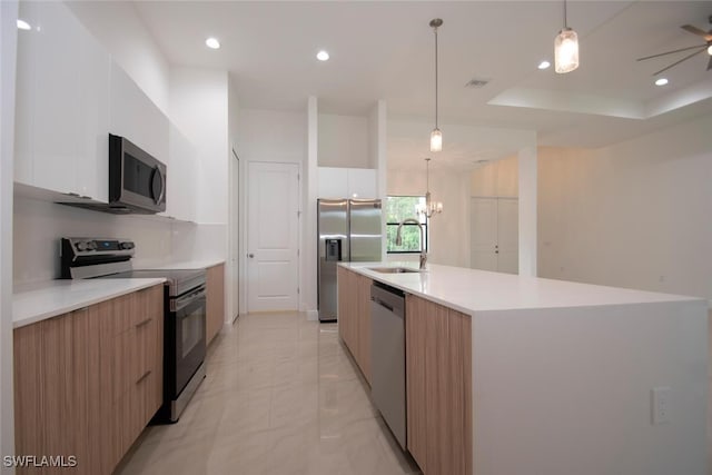 kitchen featuring white cabinetry, a kitchen island with sink, a tray ceiling, stainless steel appliances, and sink