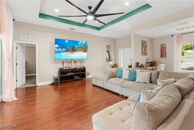 living room featuring wood-type flooring, a tray ceiling, and ceiling fan