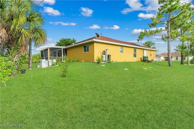 rear view of property with cooling unit, a sunroom, and a lawn