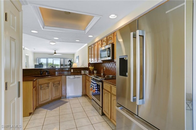 kitchen featuring light tile patterned floors, a raised ceiling, dark countertops, appliances with stainless steel finishes, and a sink